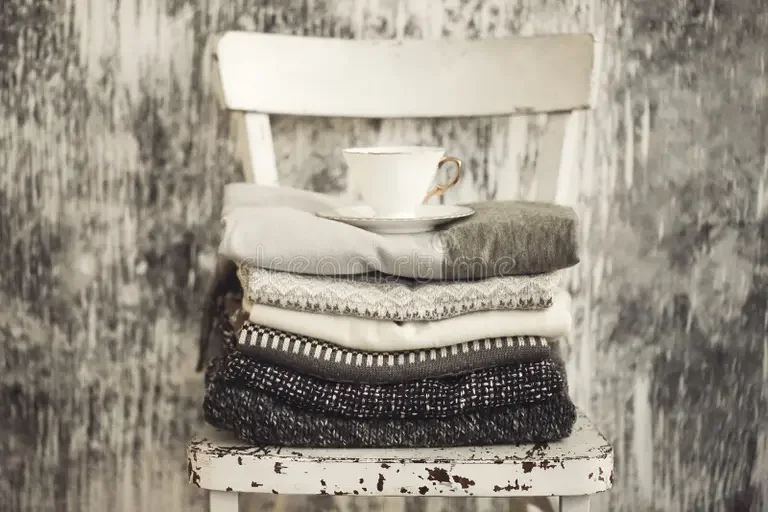 pile-knitted-warm-grey-white-blankets-scarves-woolen-sweaters-winter-fall-cold-weather-stool-near-gray-wall-165222673.webp