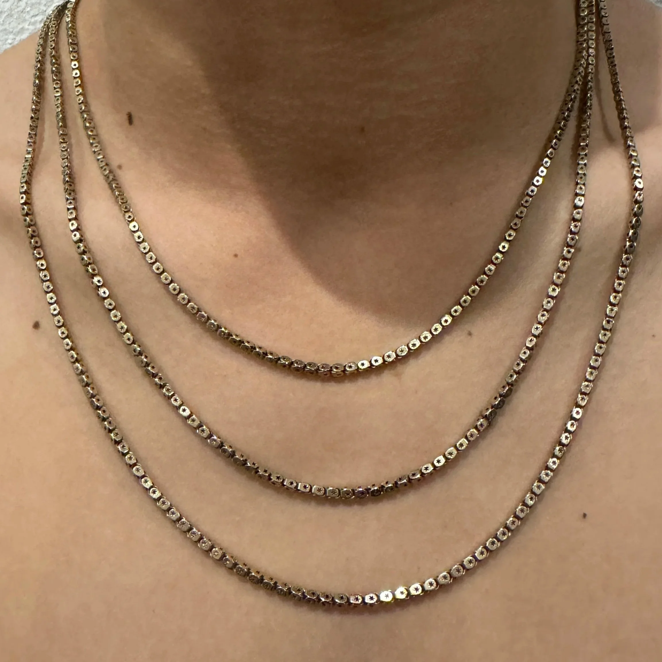 Vintage graduated box-link necklace worn layered at the neckline with three articulated strands and warm brushed gold finish