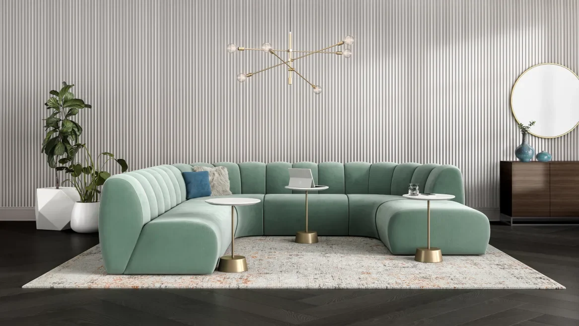 Modern living room with a large green sectional sofa, two white side tables, a laptop, glass of water, and decorative pillows, set on a light-colored rug against a textured silver wall with a gold chandelier and a mirror with vases on a wooden sideboard.