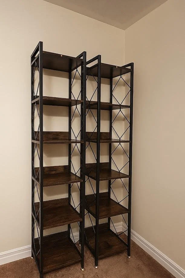 Two black metal and wood open-shelving units standing against a beige wall in a room with light-colored walls and brown carpet.