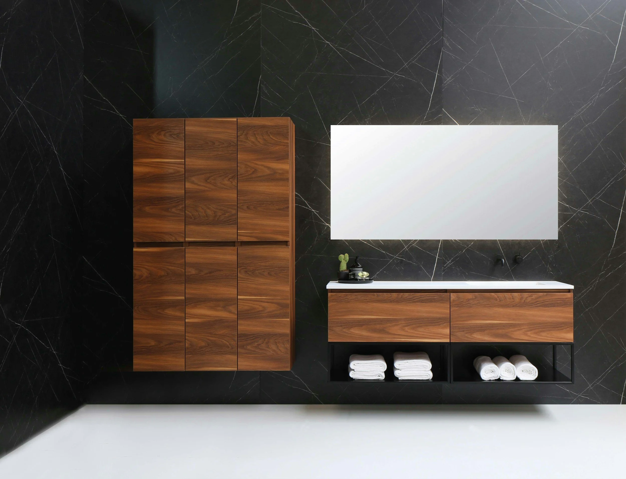 Modern bathroom with black marble walls, wooden cabinets, a large rectangular mirror, and neatly folded white towels.