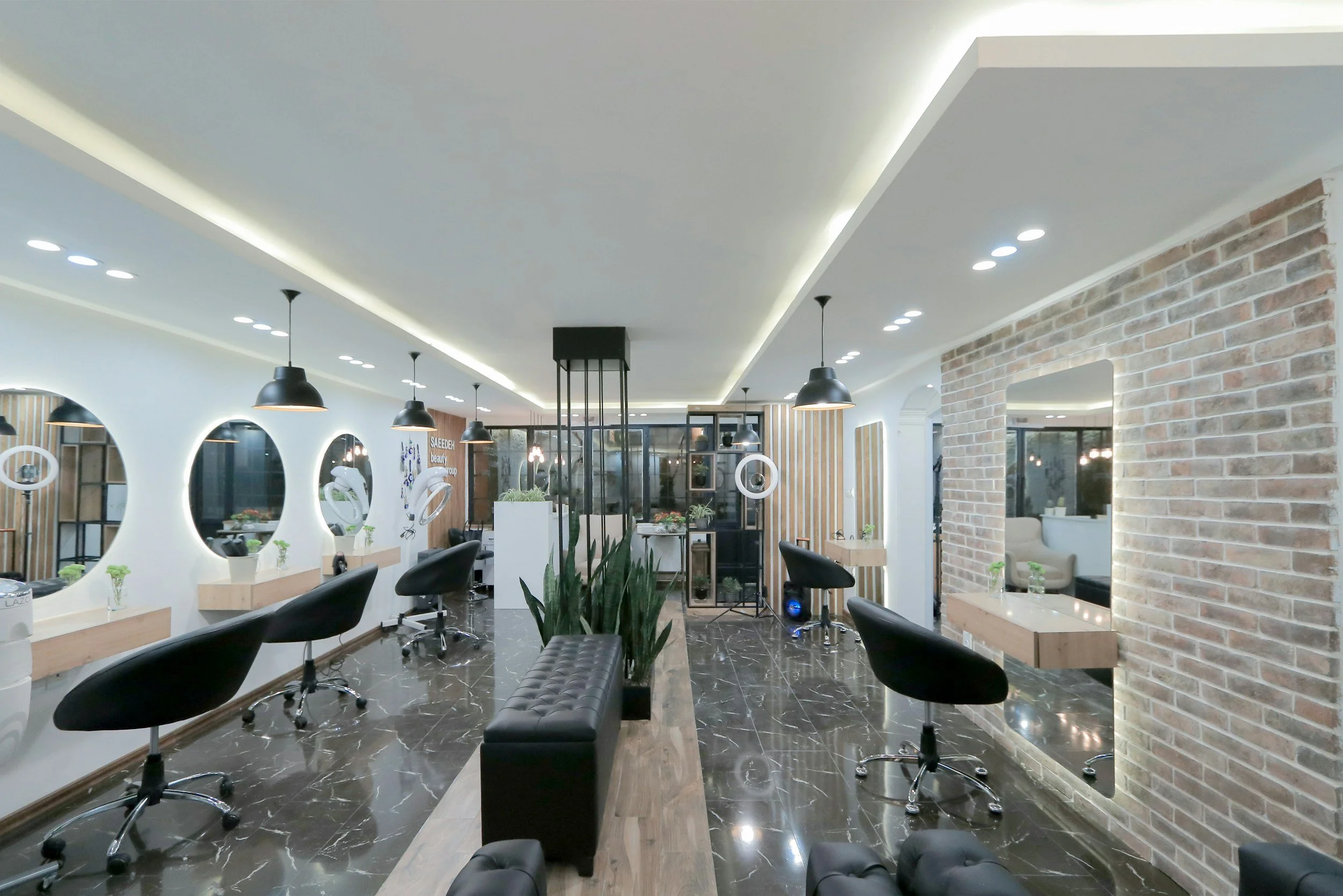 Modern hair salon with black styling chairs, circular mirrors with backlighting, black pendant lights, and a brick accent wall, featuring a polished dark marble floor and wooden accents.