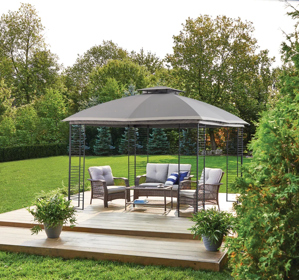 A patio with outdoor furniture beneath a large gray umbrella, surrounded by greenery and trees.