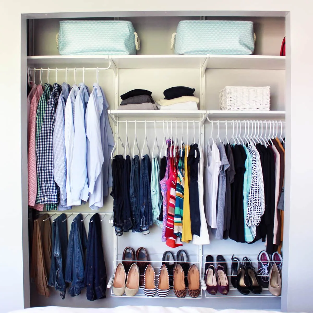 Open closet with hanging shirts, pants, and shoes, with storage baskets and folded clothes on top shelves.