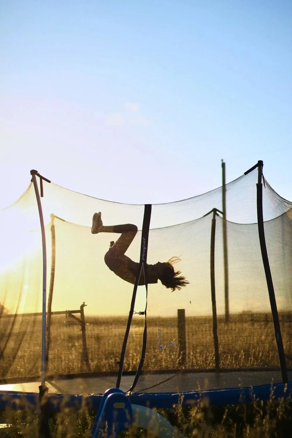 Person performing a flip inside a trampoline enclosure at sunset.
