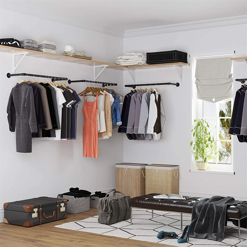 A walk-in closet with clothes hanging on black rods, shelves with folded clothes, a window with a plant, and some storage boxes on the floor.