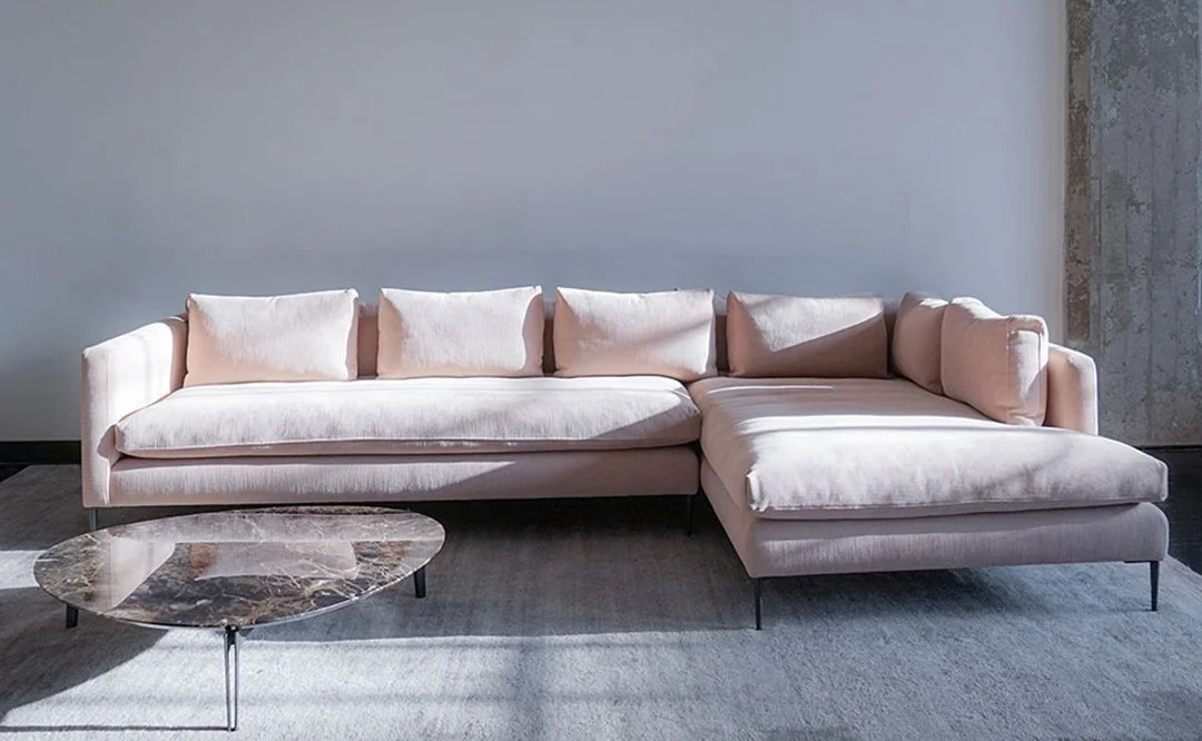 Modern light pink sectional sofa with a marble coffee table in front.