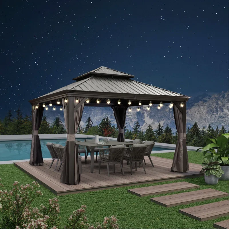Nighttime outdoor scene featuring a gazebo with a metal roof, string lights, and curtains, situated on a wooden deck beside a swimming pool, with mountains and trees in the background.