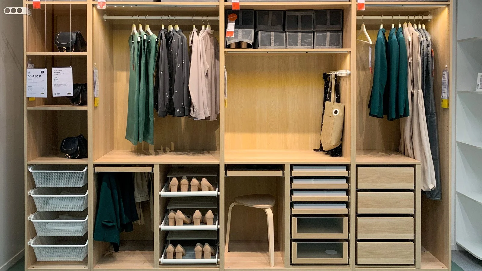 Wooden wardrobe with shelves, hanging clothes, shoes, and storage boxes, in a retail store or closet.