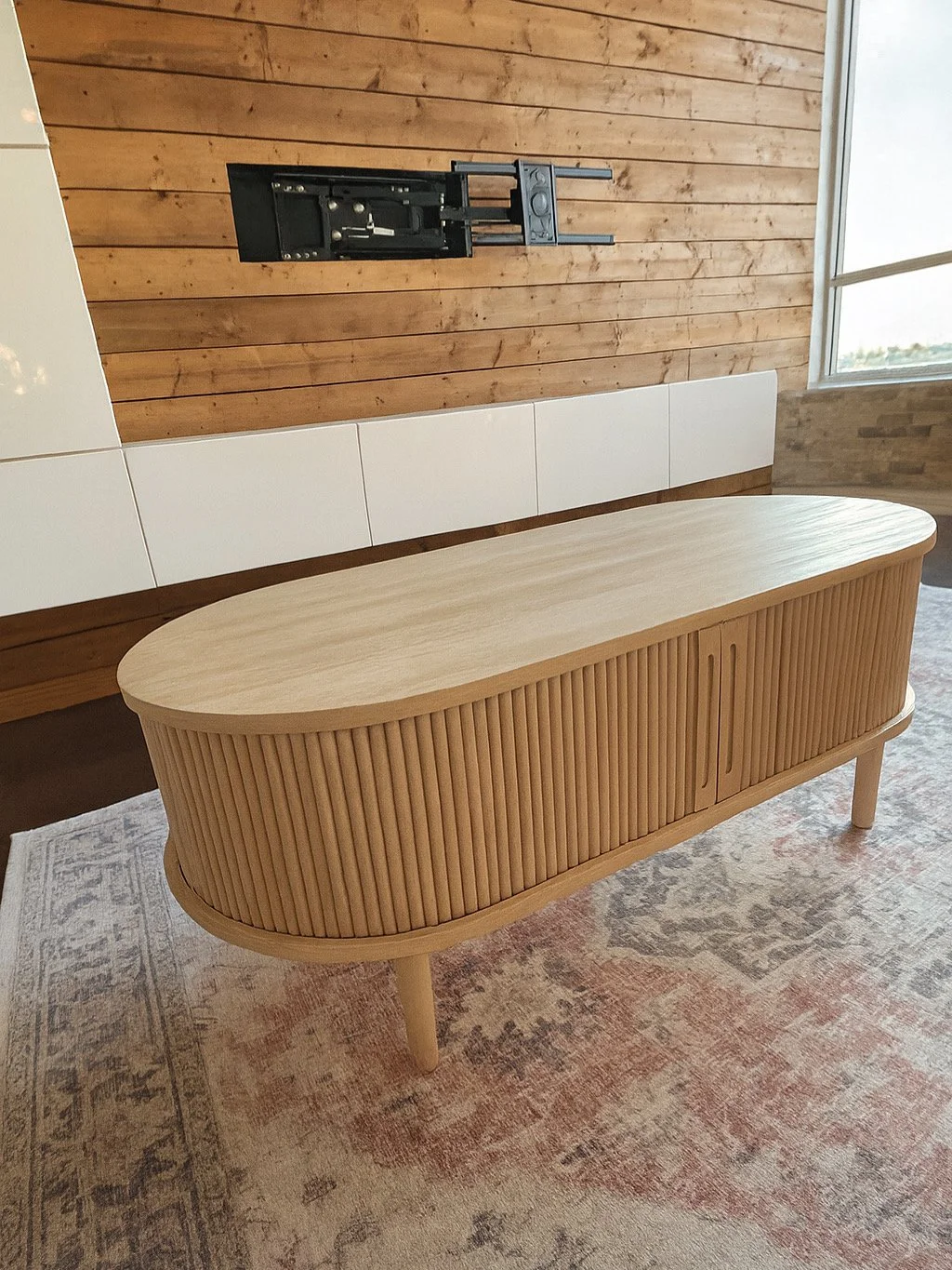 Empty wooden sideboard with curved edges in a room with a wooden wall and a window.