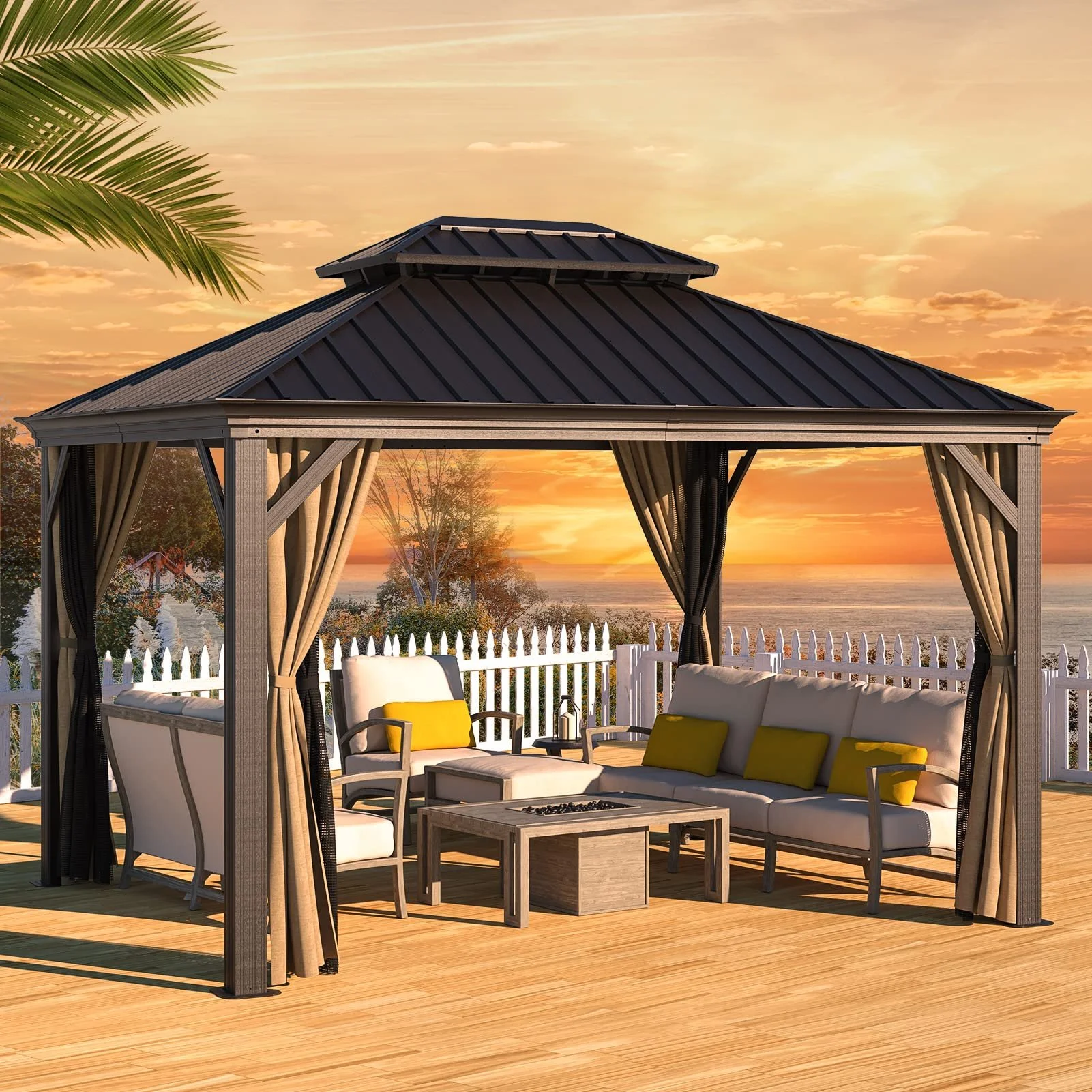 A outdoor gazebo with beige curtains and black roofing overlooking the sunset by the water, with outdoor sofa and chairs with yellow cushions and a small table.