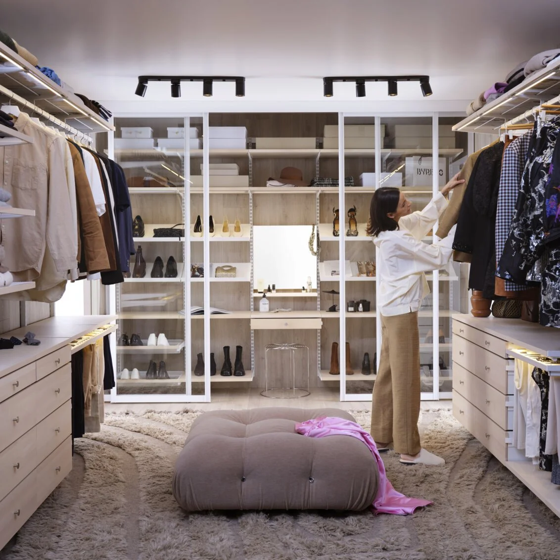 A woman shopping for clothes in her walk-in closet, reaching for a garment on a rack with shoes and accessories on shelves behind her.