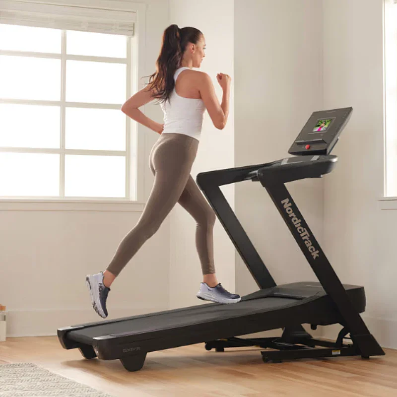 A woman jogging on a treadmill in a bright room with large windows.