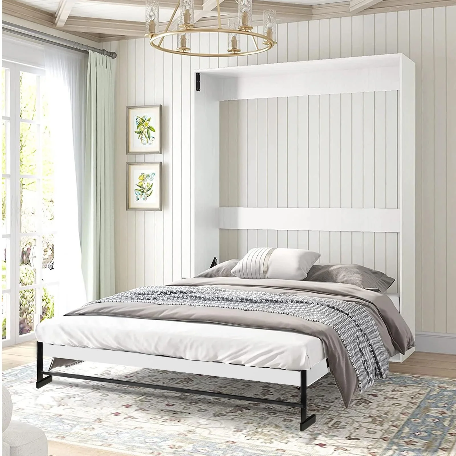 A bedroom with a white bed with gray and beige bedding and pillows, a patterned rug, large windows with white curtains, framed botanical art on the wall, and a modern chandelier hanging from the ceiling.