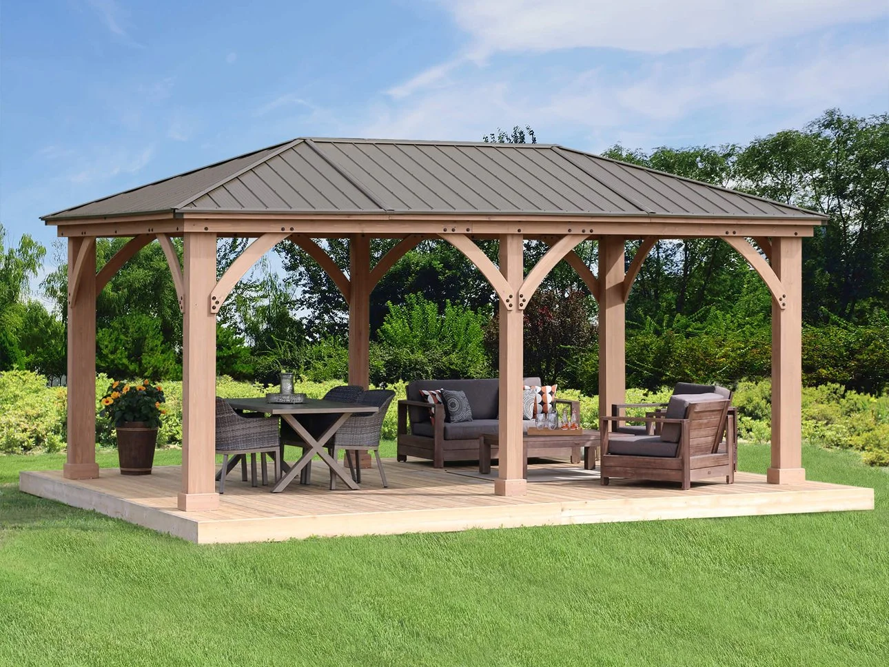 Wooden outdoor gazebo with furniture and sitting area on a grassy lawn.