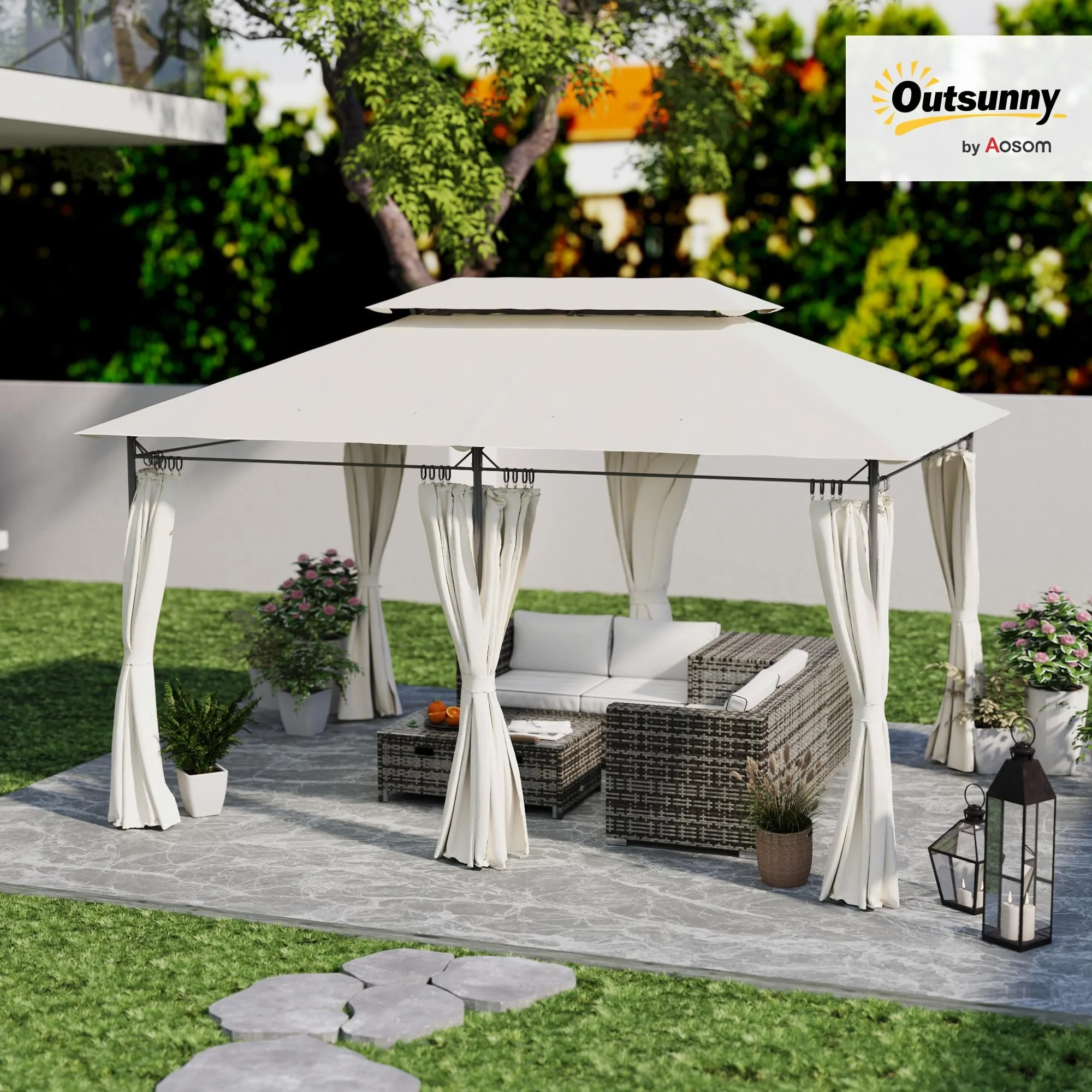 A white outdoor gazebo with curtains and a wicker seating area, situated on a patterned rug on a lawn with potted plants, flowers, and lanterns, under a tree with green foliage.