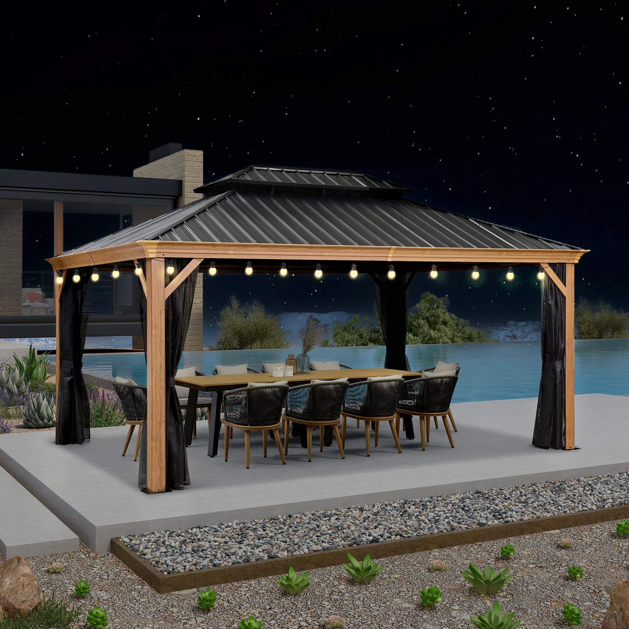 Outdoor dining area under a gazebo with string lights at night, next to a pool, with plants and landscape in the background.