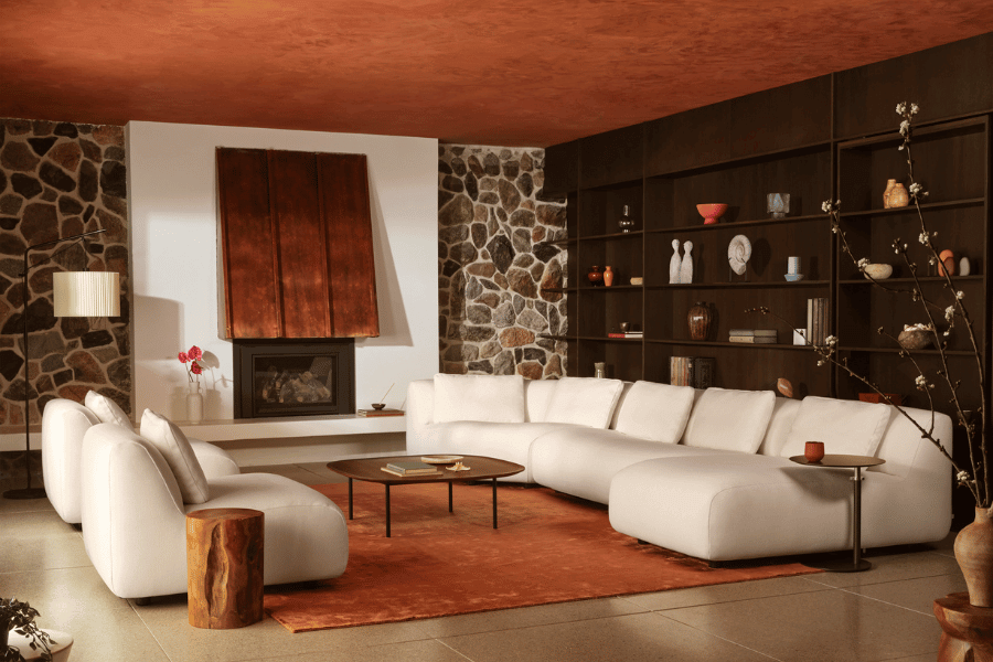 Cozy living room with a white sectional sofa, a wooden coffee table, a stone fireplace, dark built-in shelves with decorative items, and a rust-colored area rug.