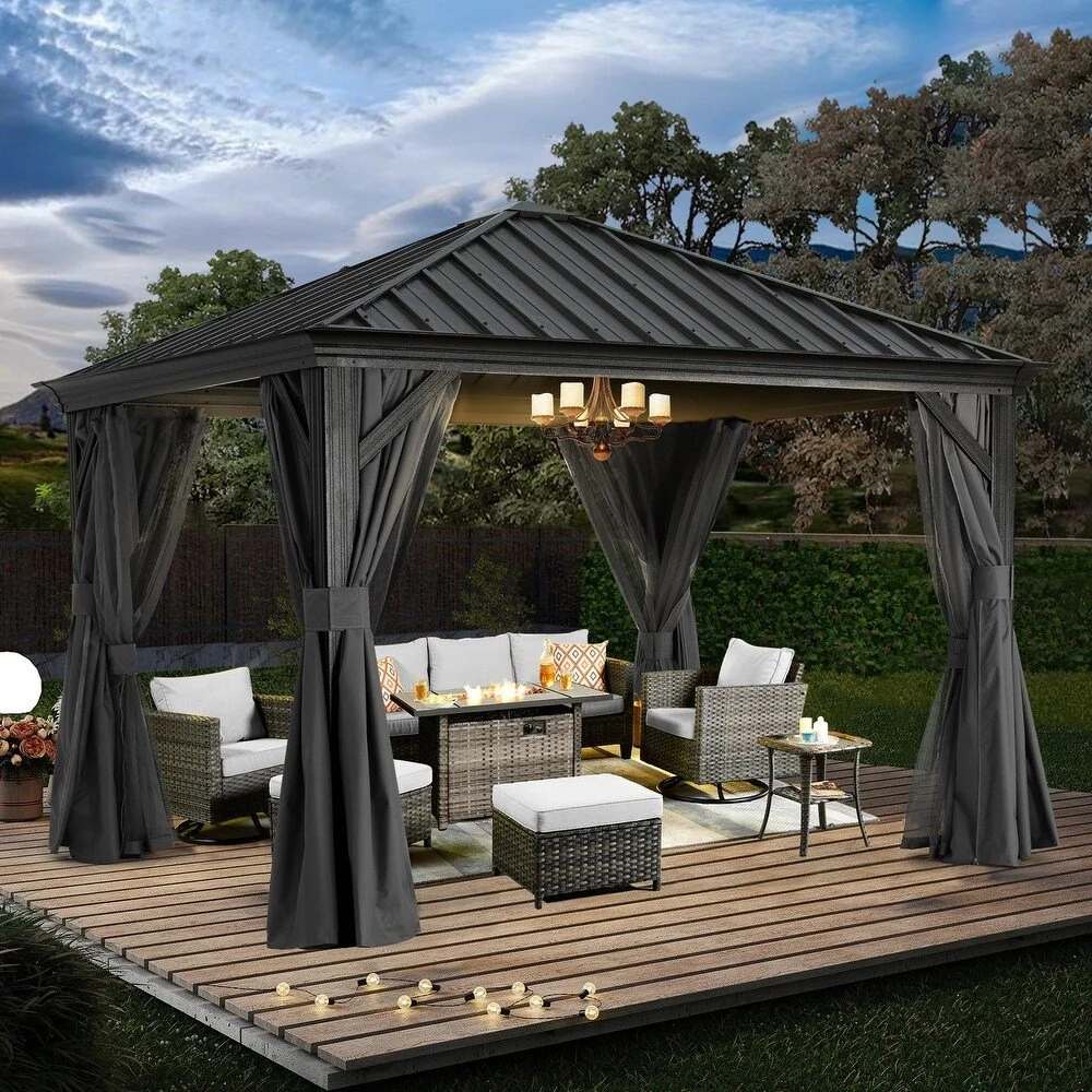 Outdoor patio with a black cabana, white cushioned seating, a coffee table with a lit fire pit, and string lights on a wooden deck, with trees and a partly cloudy sky in the background.