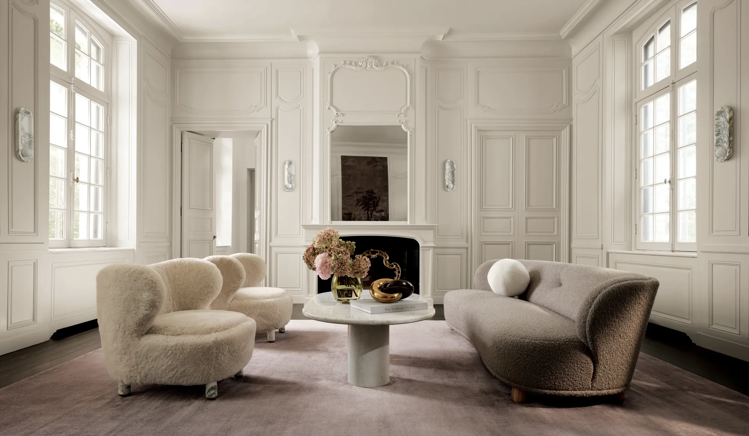 Elegant living room with cream and beige furniture, white paneled walls, and large windows.