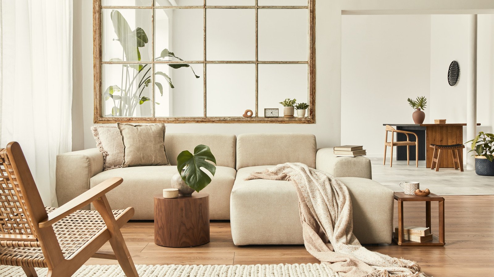 Bright living room with beige sofa, wooden side table, houseplants, large window, and simple decor with neutral tones.