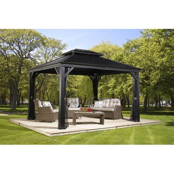Outdoor gazebo with black metal roof and wooden support beams in a green park, furnished with wicker sofas and a coffee table.