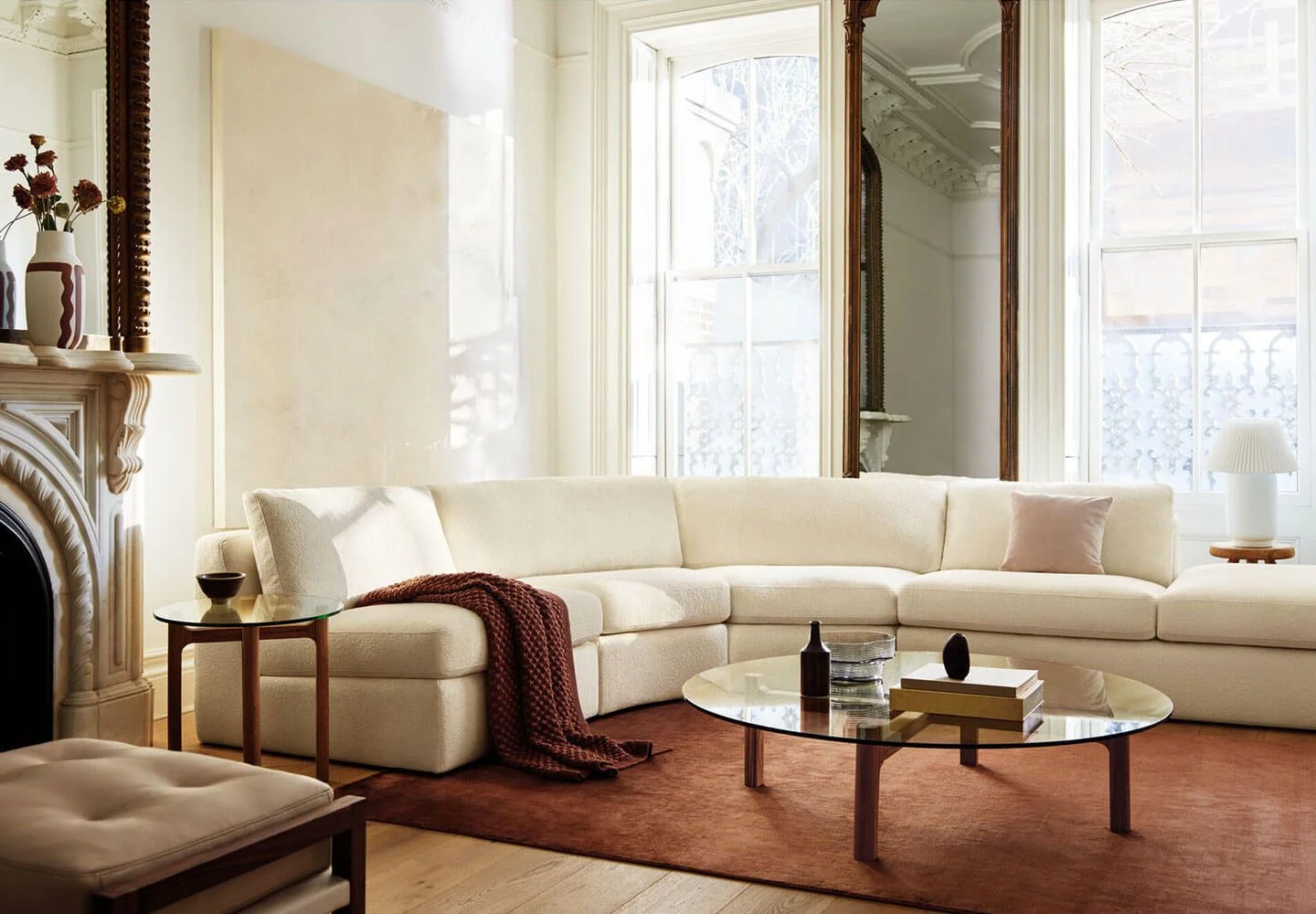 A bright living room with a large white sectional sofa, a glass coffee table, and large windows letting in natural light.