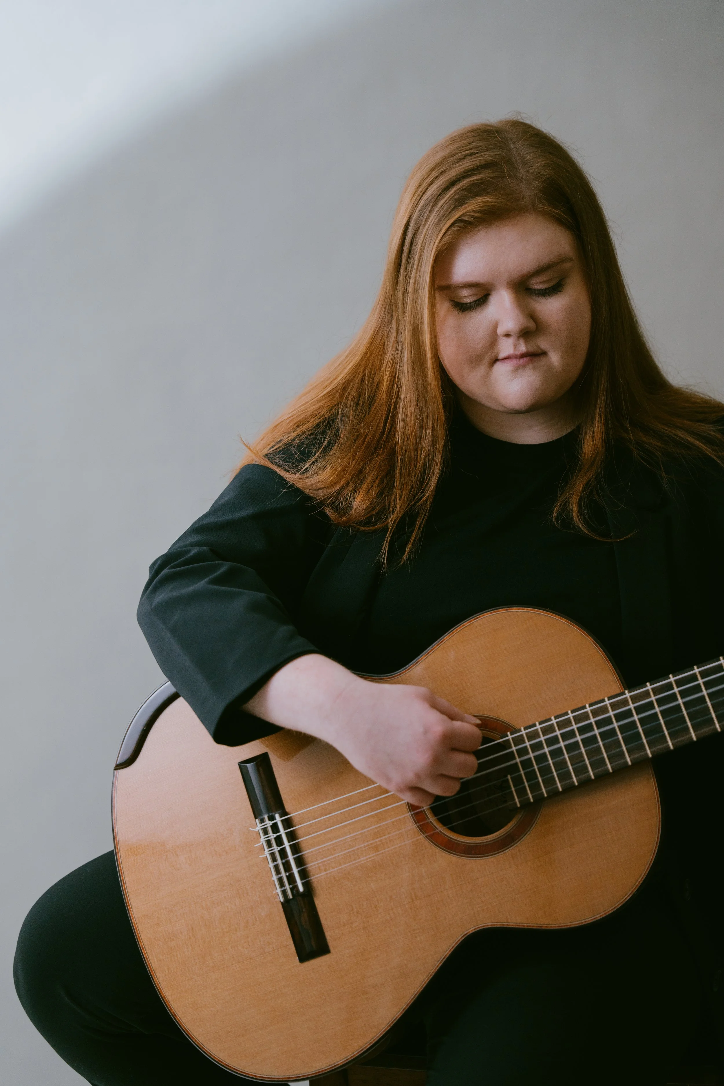 A woman with long red hair playing a classical guitar.