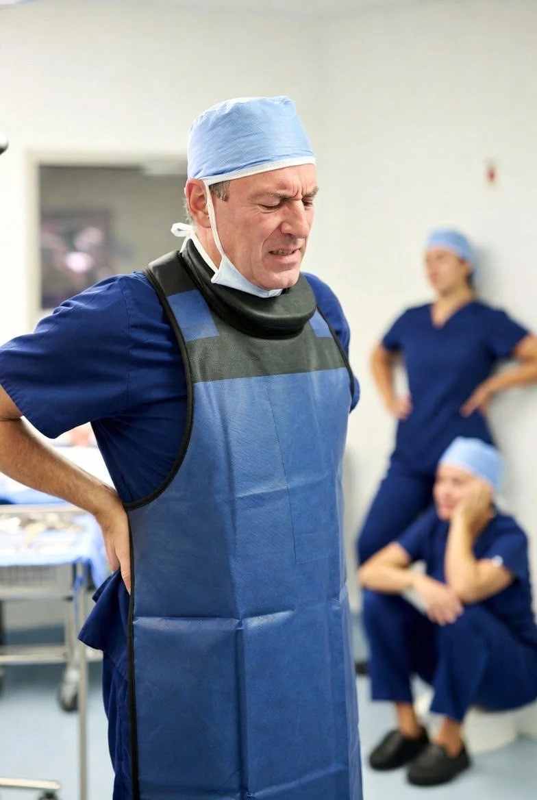 Doctor in operating room wearing a lead apron and holding his back in pain