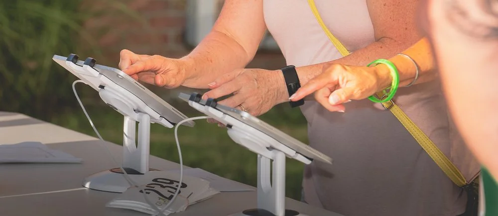 People using touchscreen tablets at an outdoor event or market stand.