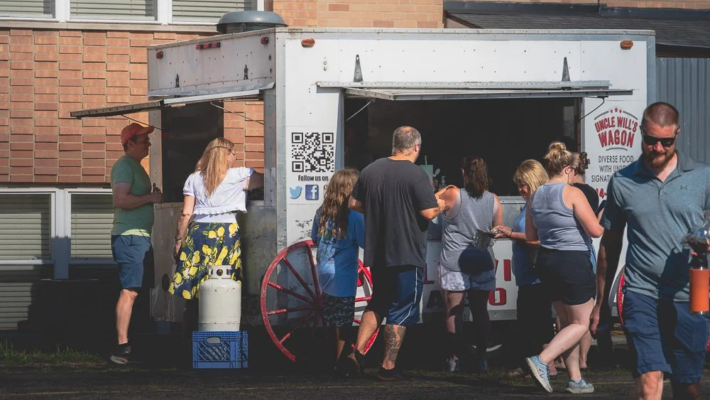 People lined up at a food truck called Uncle Will's Wagon, serving diverse food, during daytime.