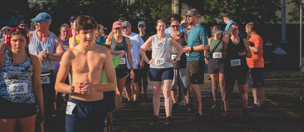 Group of people standing together at the starting line of a race, wearing athletic clothing and race bibs.