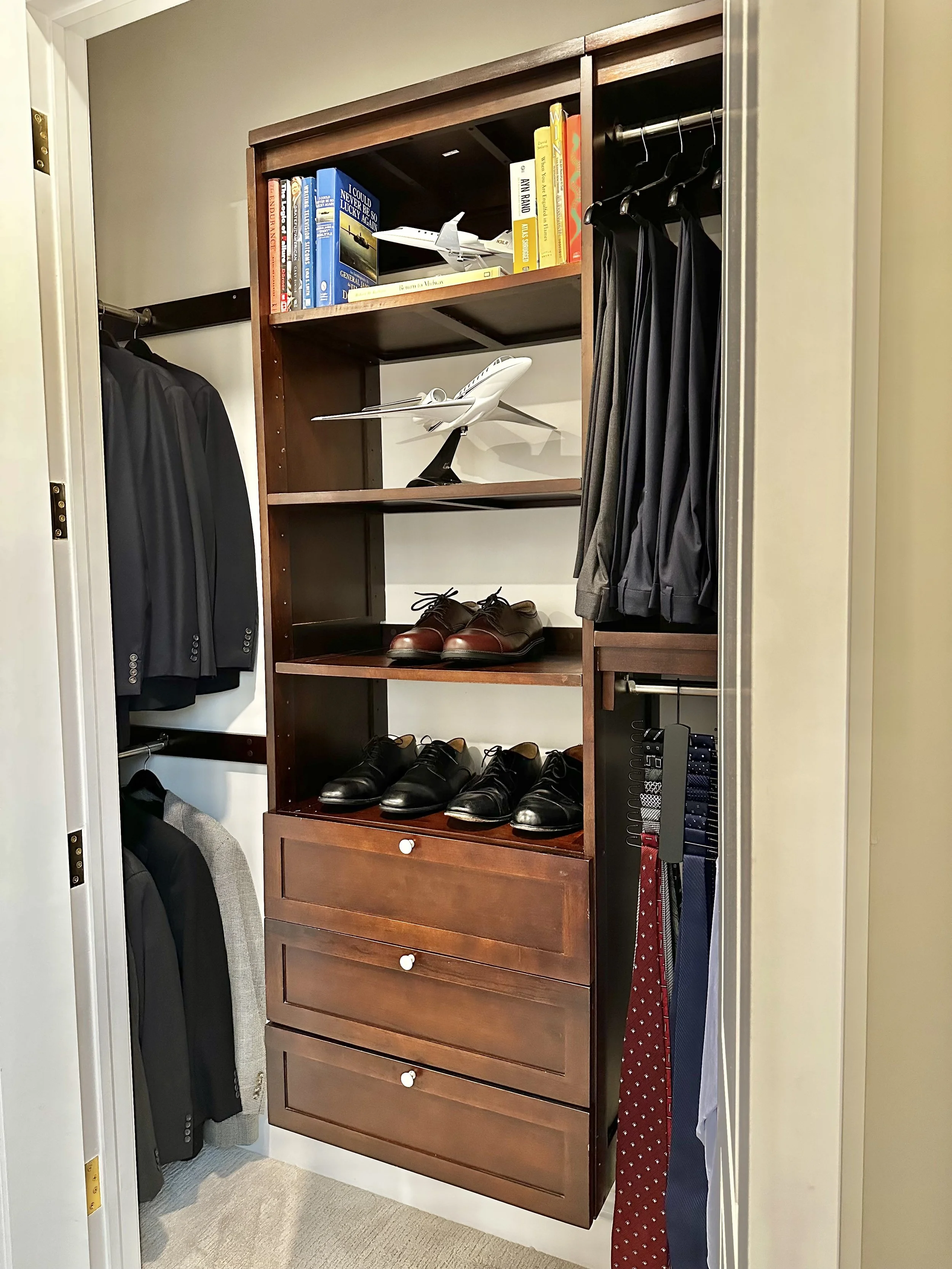A closet with suits, shoes, books, and model airplanes.