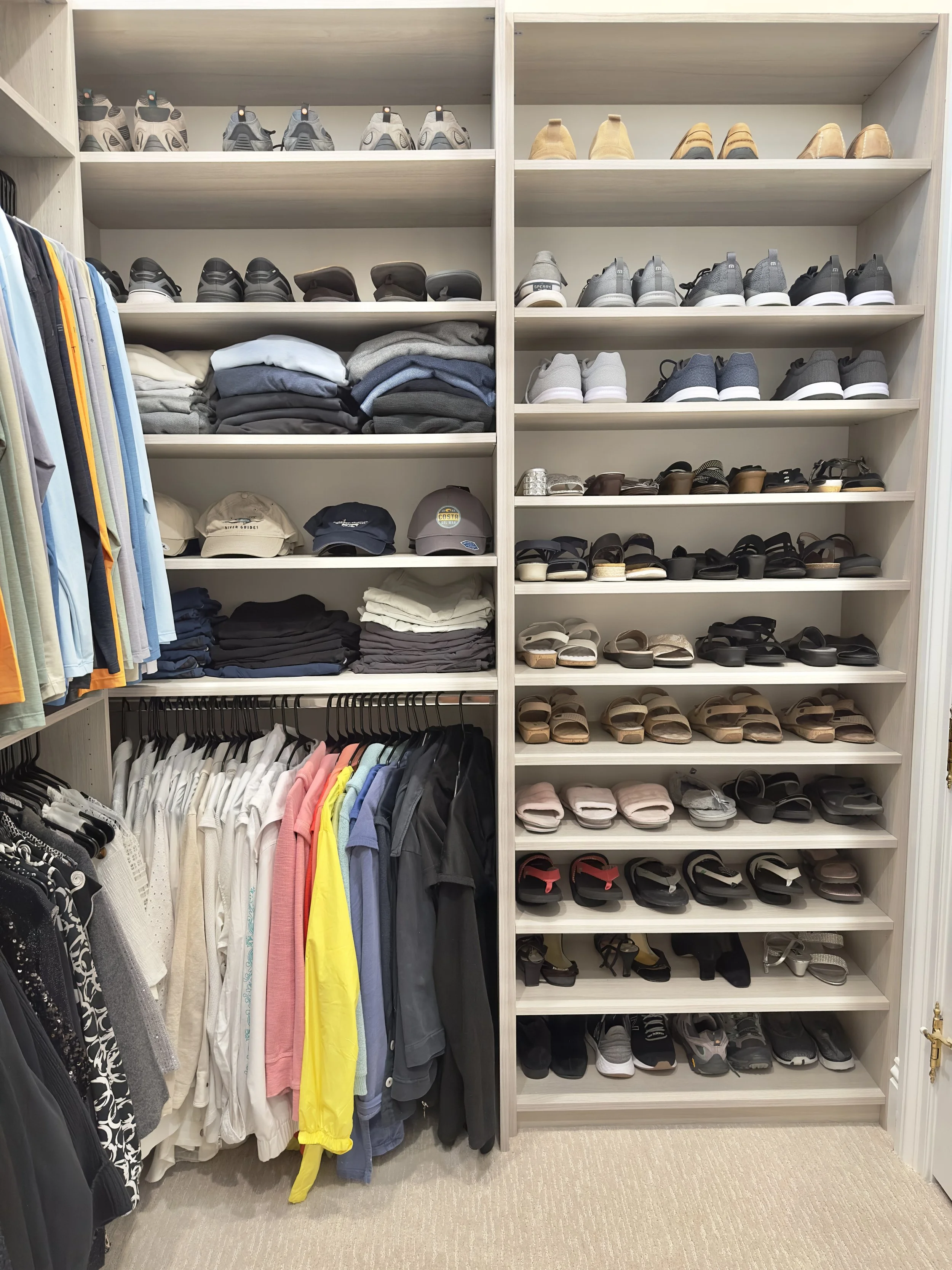Clothing closet with shelves of shoes, hats, folded clothes, and hanging shirts and jackets.
