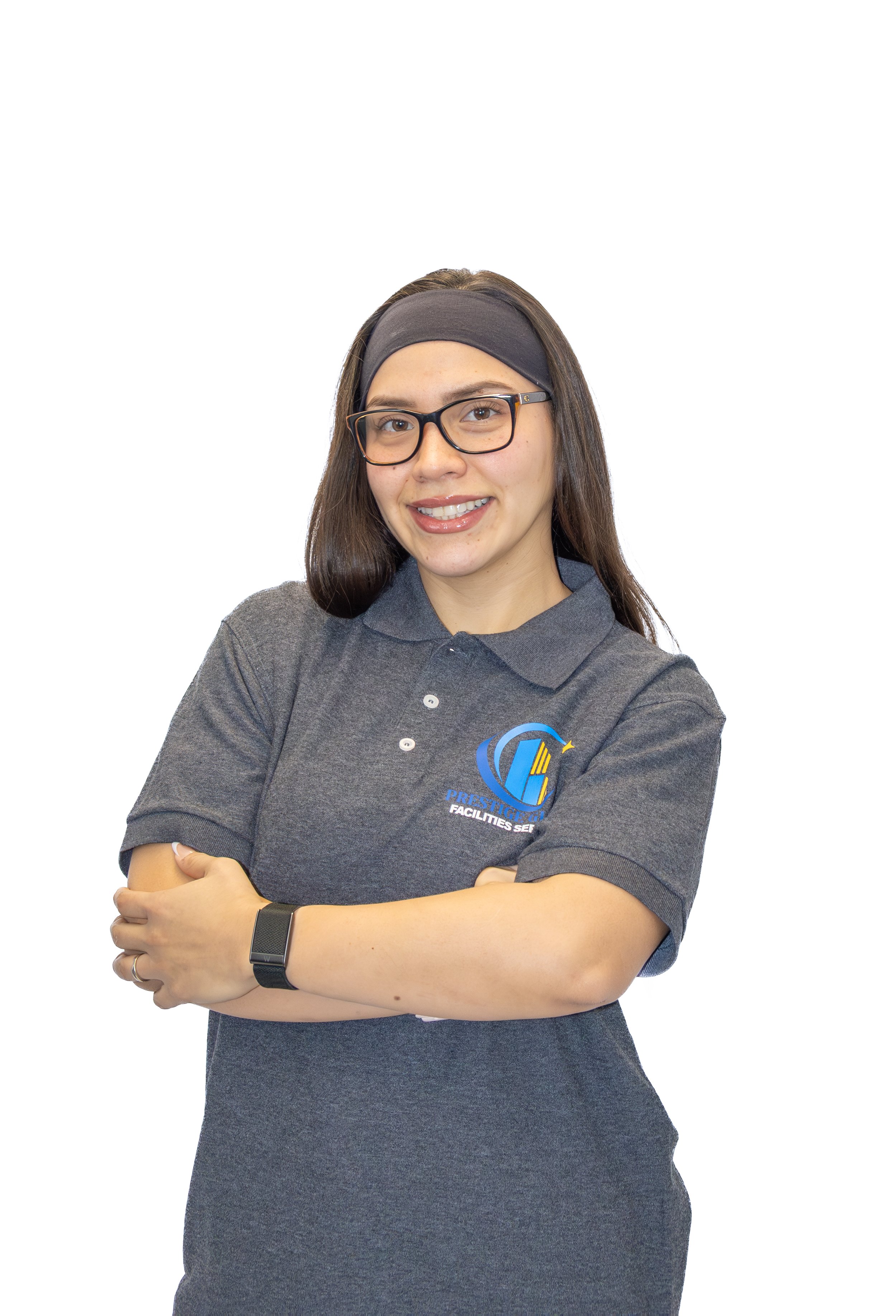 A woman with glasses, long brown hair, and a gray headband, wearing a gray polo shirt with a logo on it, standing with her arms crossed, smiling at the camera.