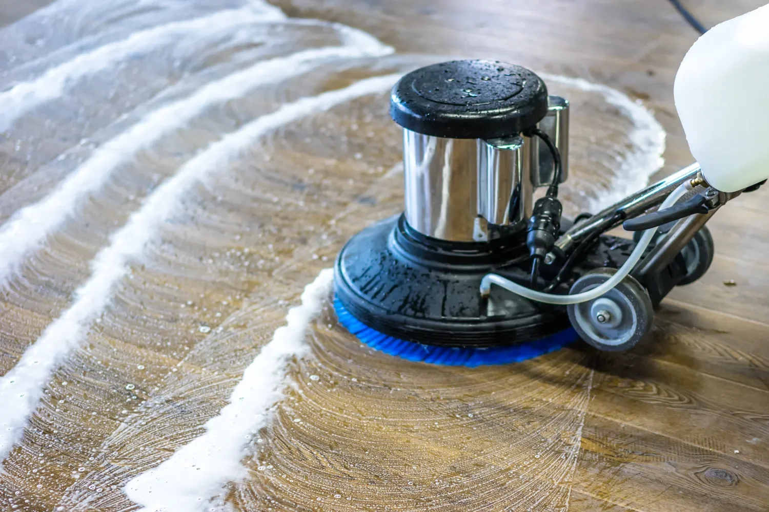 A floor buffer cleaning a hardwood floor, leaving behind a streak of foam.