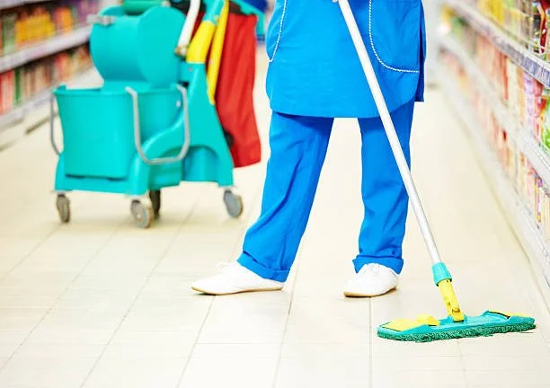 Person in blue uniform cleaning supermarket floor with a mop