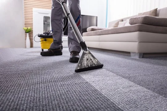 Person vacuuming carpet with a modern vacuum cleaner in a living room.