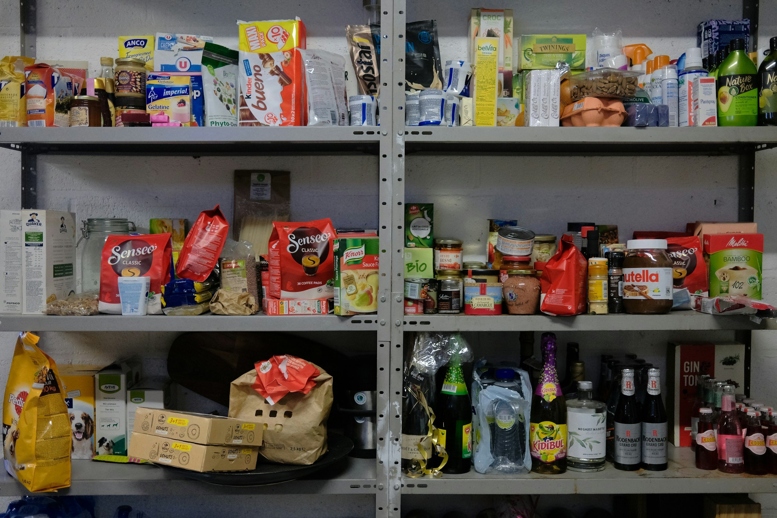 Shelves stocked with various food and household items, including pet food, canned goods, bottles, packaged snacks, and cleaning supplies.
