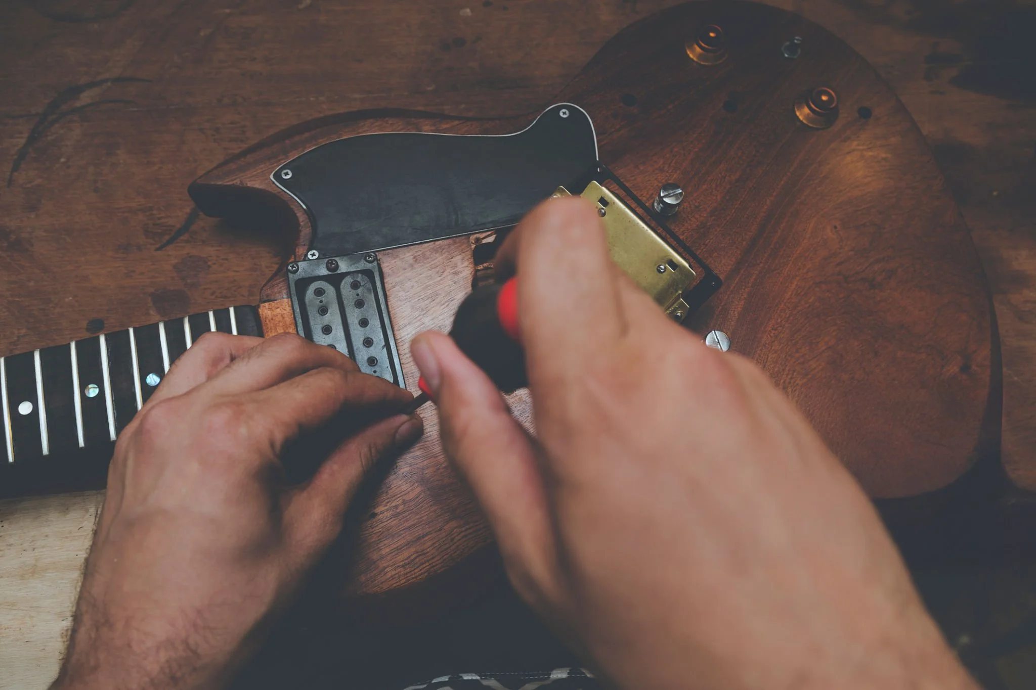 Person working on assembling the back of an electric guitar, focusing on the area where the electronics and components are installed, with a wooden surface underneath.