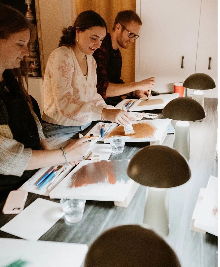 People painting on canvases at a table during an art class.