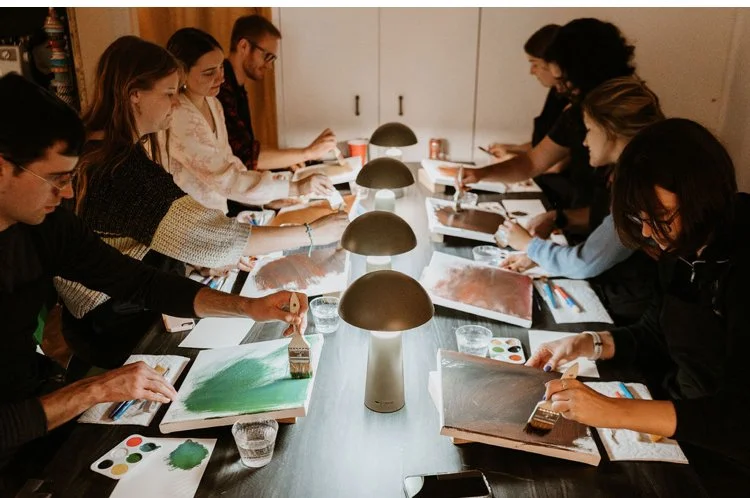 Group of nine people painting on canvases around a table