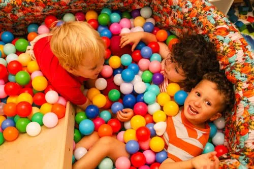 Two young children playing in a colorful ball pit, smiling and having fun.