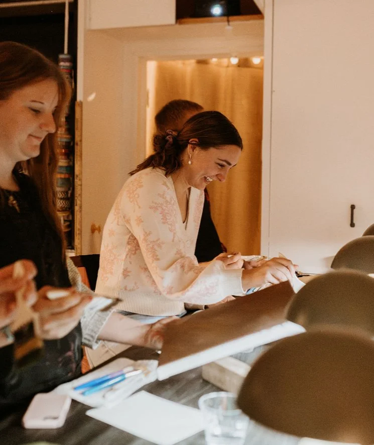 Women laughing and engaging with their phones at a counter in a warmly lit room.