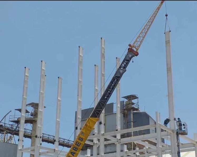 Construction site with a crane lifting a metal beam among tall vertical supports in progress.