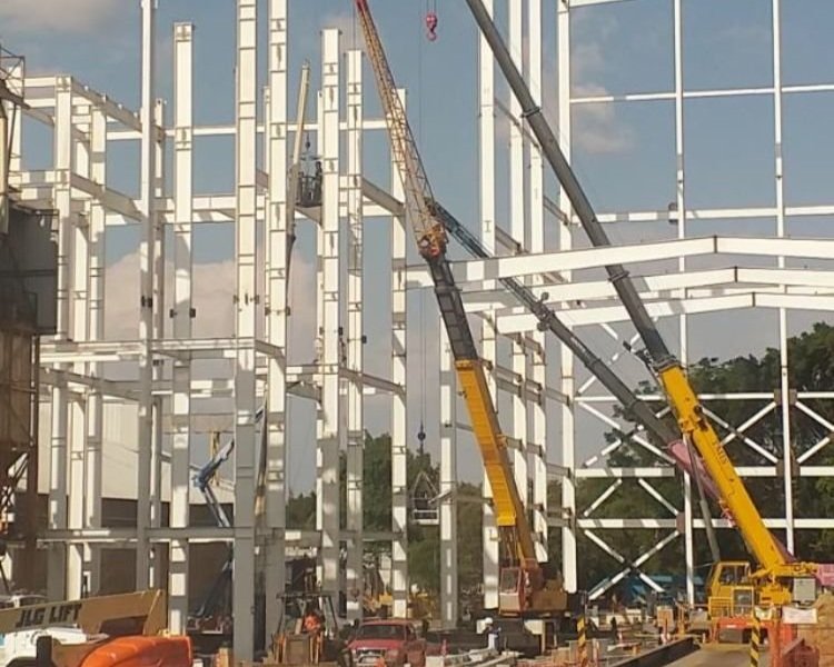 Construction site with multiple cranes lifting large white steel beams for building framework