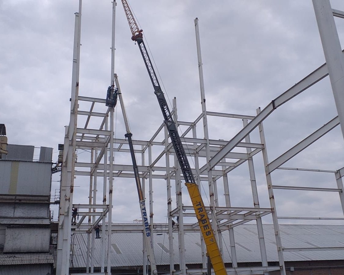 Two cranes working on a steel building framework during construction on a cloudy day.