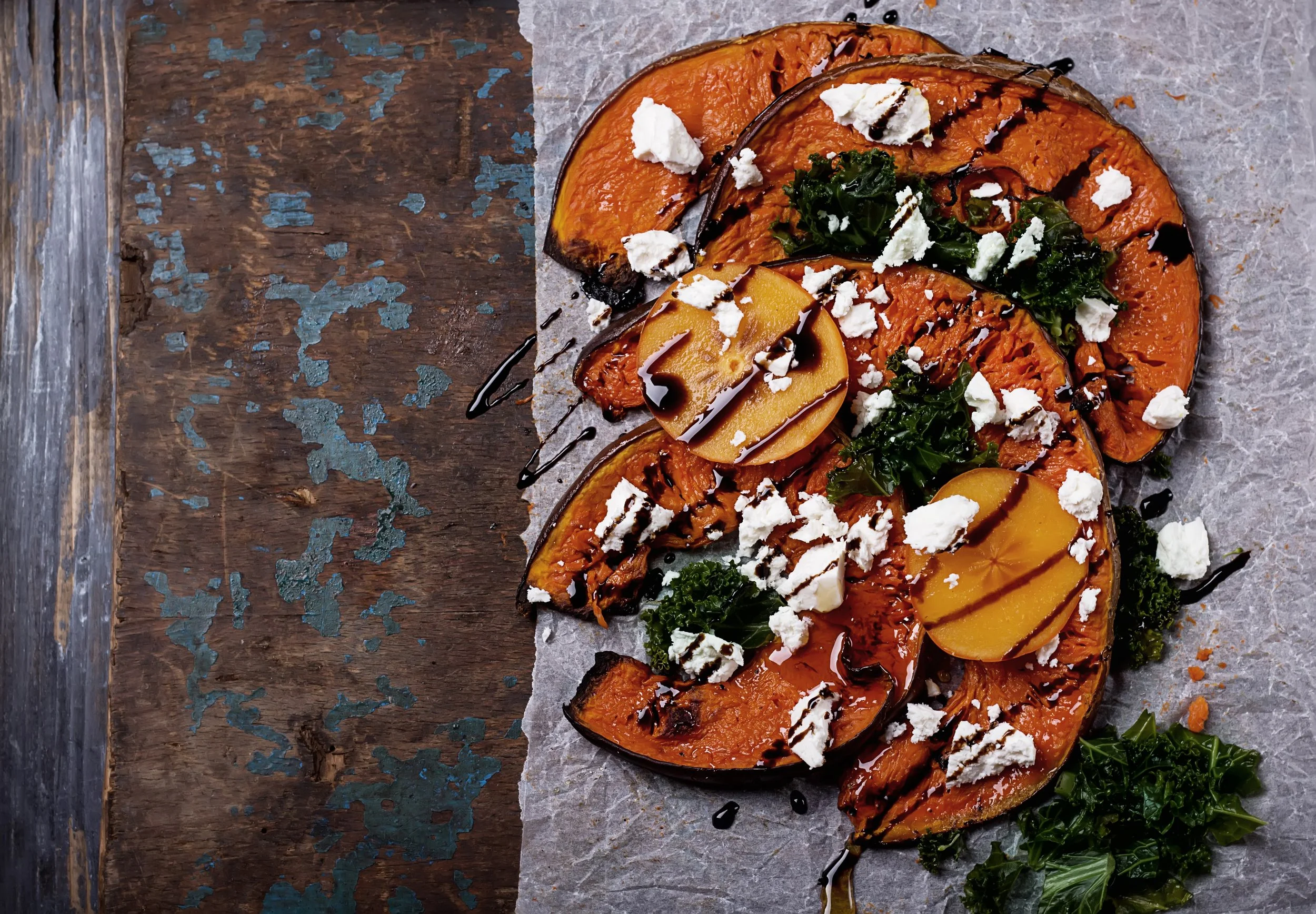Roasted acorn squash slices topped with crumbled cheese, drizzled with balsamic glaze, served on parchment paper