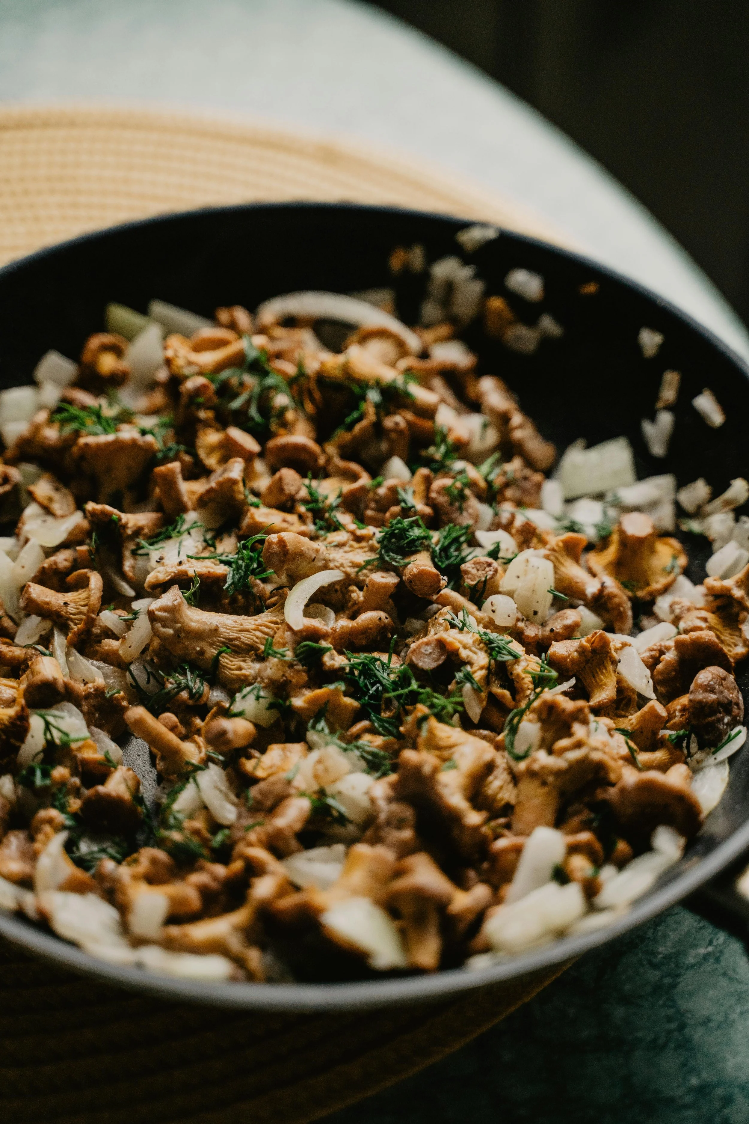 Cooked chopped mushrooms with chopped onions and fresh herbs in a black skillet.