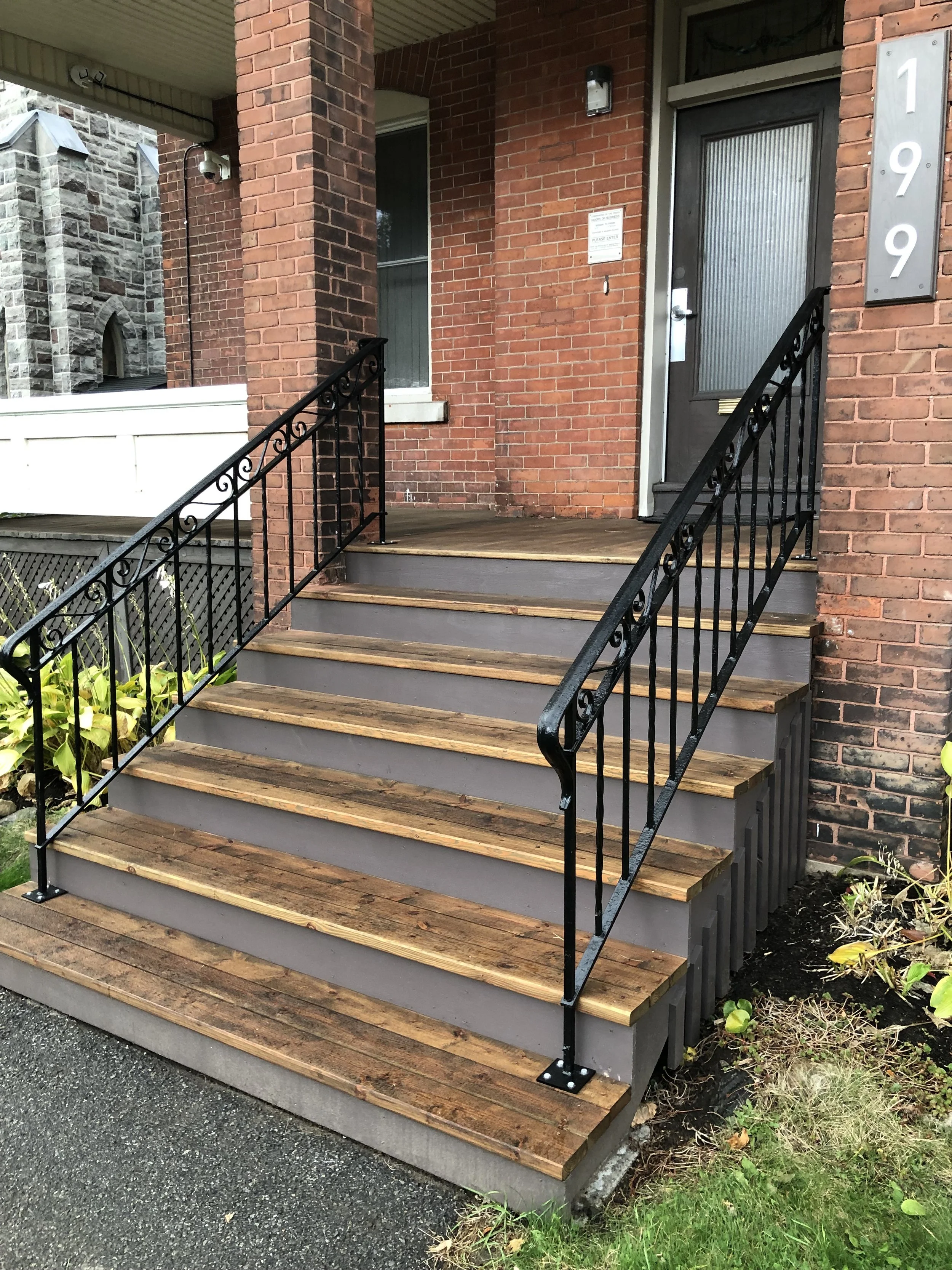 Refurbished front porch of a brick building with stairs, black metal railing, and a gray door.